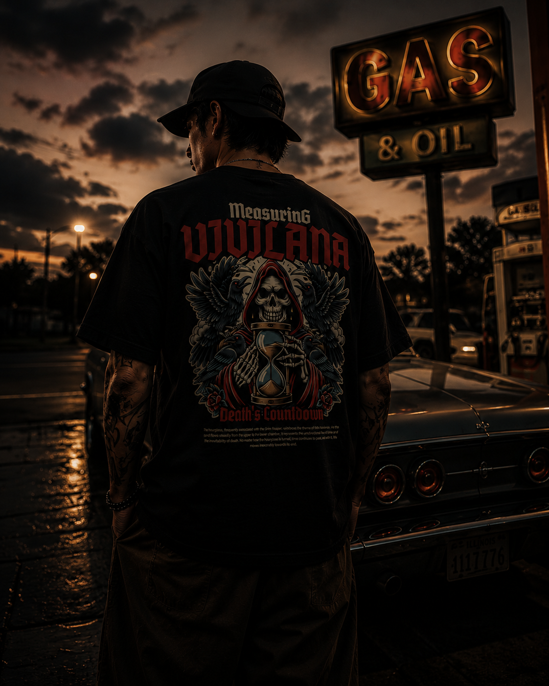 Man wearing black graphic tee with skull, ravens, and hourglass design at gas station dusk