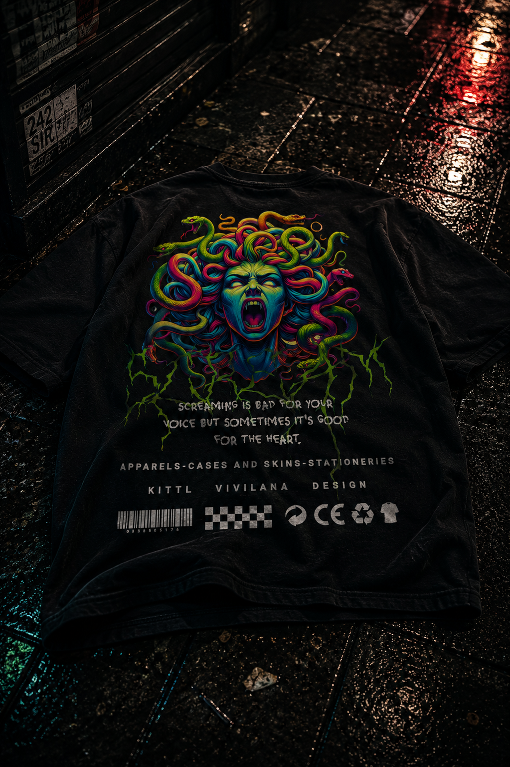 Black graphic tee with vibrant Medusa print, screaming face, and bold text on wet urban street.